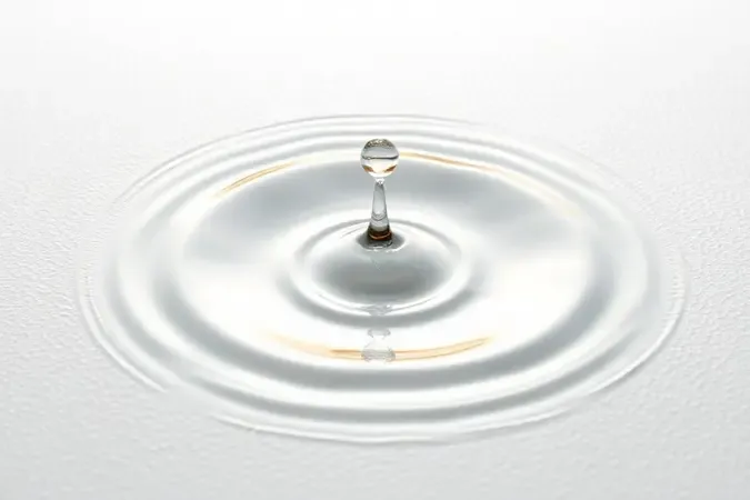 Close conceitual de uma gota de líquido atingindo uma superfície branca texturizada com efeito de ondulação estética.